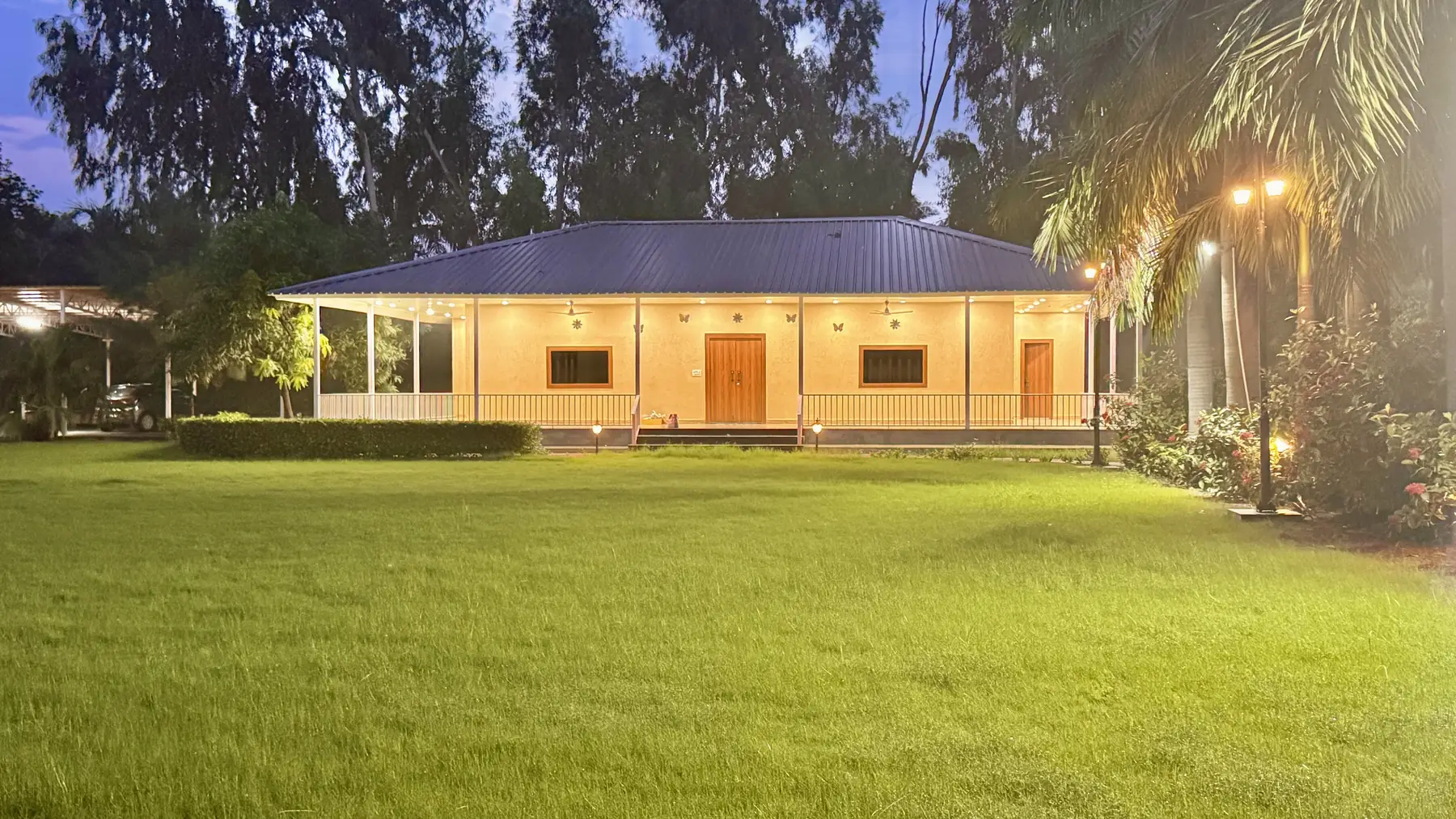 Mulberry Farm farmhouse in Noida lit at night, seen across the lawn